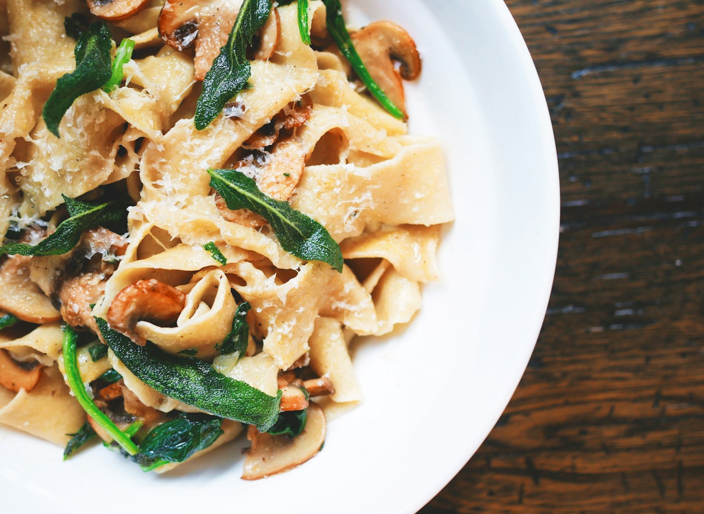 Plato hondo con pasta de cinta ancha, setas salteadas, hojas de salvia crujientes y queso rallado