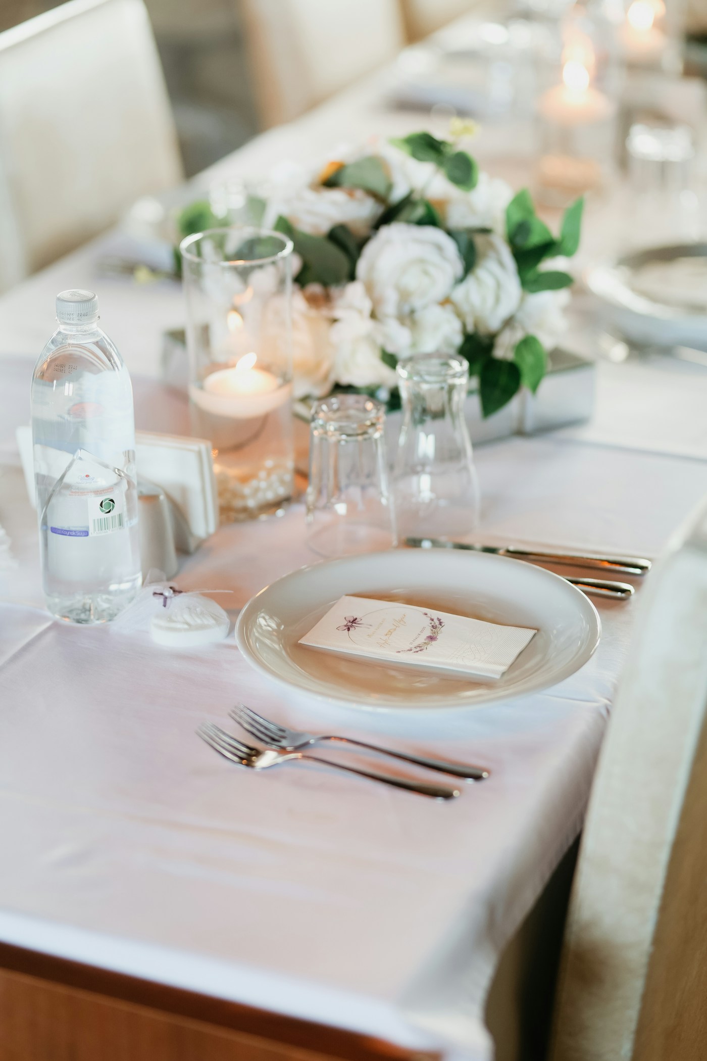 Mesa de banquete vestida con mantelería blanca, cristalería, vela encendida y centros de flores